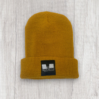 Mustard yellow beanie with a black label on a light wooden surface